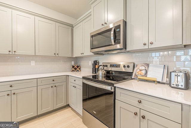 kitchen featuring tasteful backsplash, light wood-type flooring, gray cabinets, appliances with stainless steel finishes, and light countertops