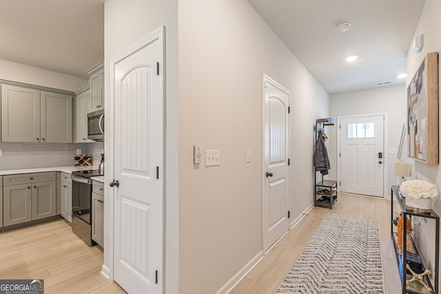 hallway with light wood finished floors, baseboards, visible vents, and recessed lighting
