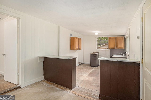 kitchen featuring light countertops, a peninsula, brown cabinets, and a sink