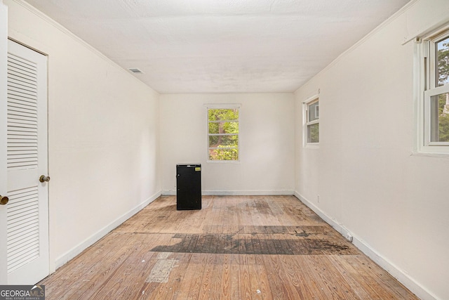 unfurnished room with crown molding, visible vents, wood-type flooring, and baseboards