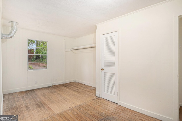 unfurnished bedroom featuring a closet, wood-type flooring, ornamental molding, and baseboards