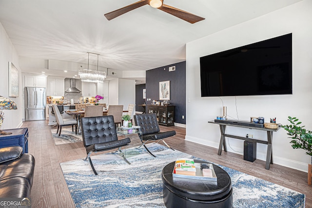 living area featuring wood finished floors, baseboards, and ceiling fan with notable chandelier