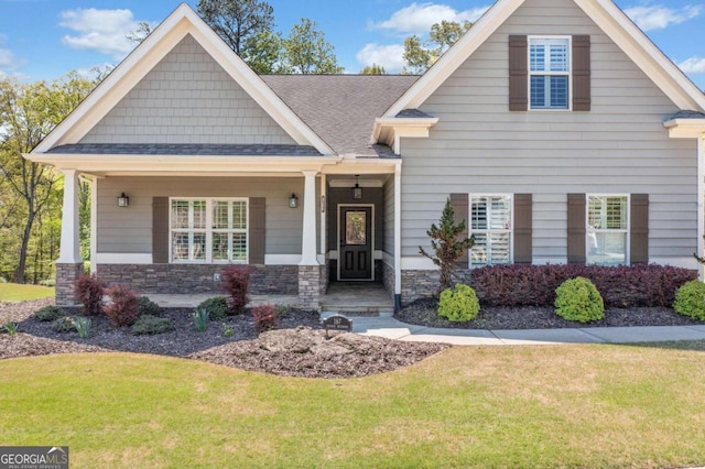 craftsman-style house with stone siding, a shingled roof, and a front yard