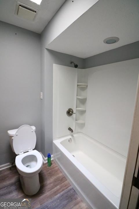 bathroom featuring wood finished floors, washtub / shower combination, toilet, and baseboards