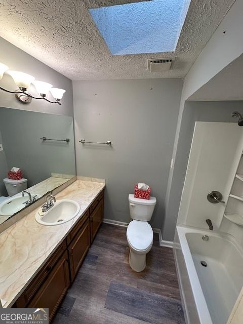 full bath with wood finished floors, vanity, a textured ceiling, toilet, and a skylight
