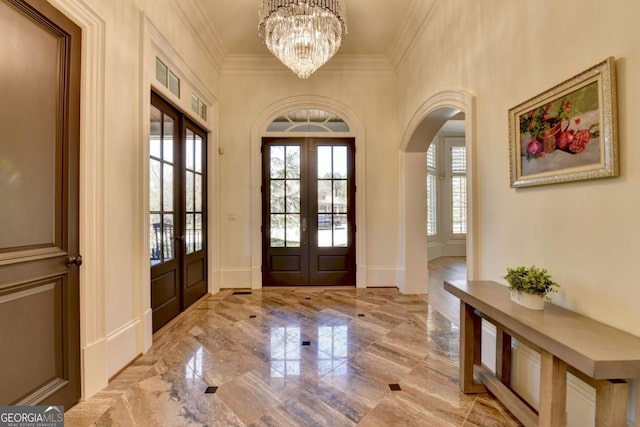 entrance foyer featuring a chandelier, french doors, crown molding, arched walkways, and marble finish floor