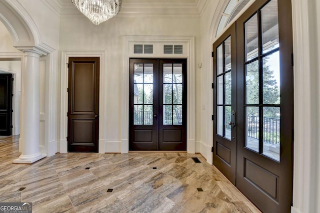 entryway with crown molding, french doors, decorative columns, and a notable chandelier