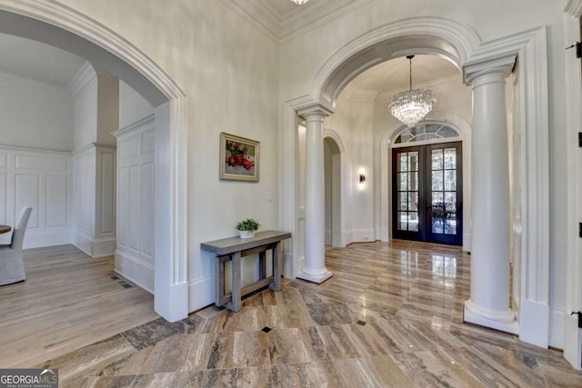 foyer entrance featuring a decorative wall, french doors, ornate columns, and arched walkways
