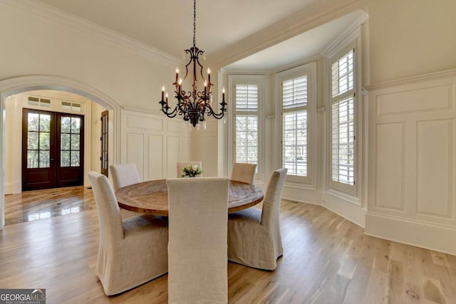 dining room with crown molding, a decorative wall, arched walkways, french doors, and a notable chandelier