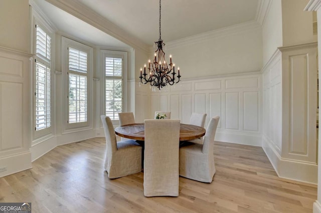 dining space featuring a decorative wall, light wood-type flooring, an inviting chandelier, and crown molding