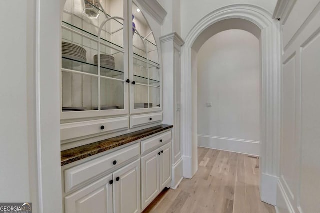bar featuring arched walkways, light wood-style floors, and baseboards