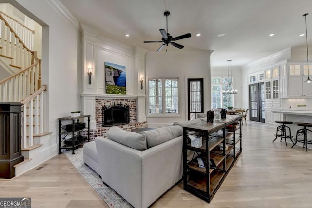 living area with ceiling fan with notable chandelier, light wood-style flooring, ornamental molding, recessed lighting, and stairs