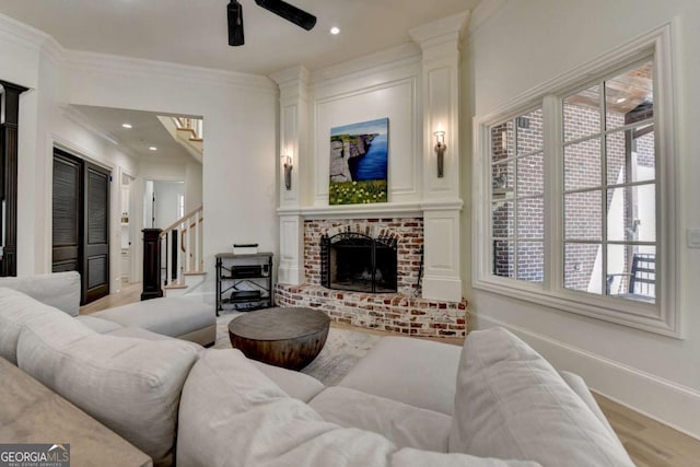 living room featuring baseboards, ornamental molding, a fireplace, stairway, and a ceiling fan