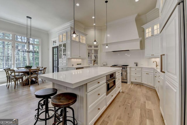 kitchen featuring light wood-style floors, premium range hood, crown molding, and appliances with stainless steel finishes