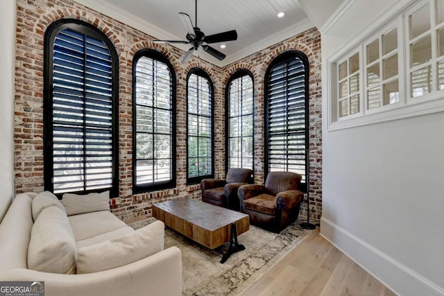 living room featuring brick wall, ceiling fan, baseboards, and wood finished floors