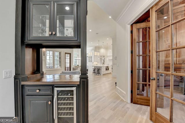 bar with light wood-style flooring, ornamental molding, beverage cooler, french doors, and baseboards
