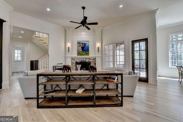 living area featuring a fireplace, stairs, light wood-style floors, and plenty of natural light