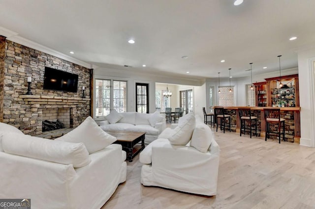 living area featuring crown molding, light wood-type flooring, a stone fireplace, and recessed lighting