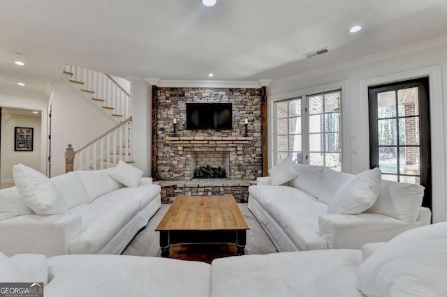 living area featuring stairway, visible vents, a stone fireplace, and crown molding