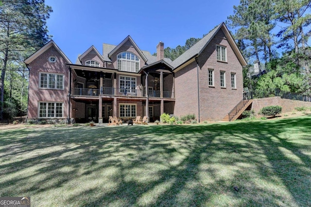 back of house featuring a patio, a chimney, stairs, brick siding, and a yard