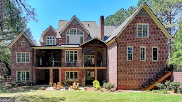 rear view of house with a balcony, a chimney, a patio area, brick siding, and a lawn