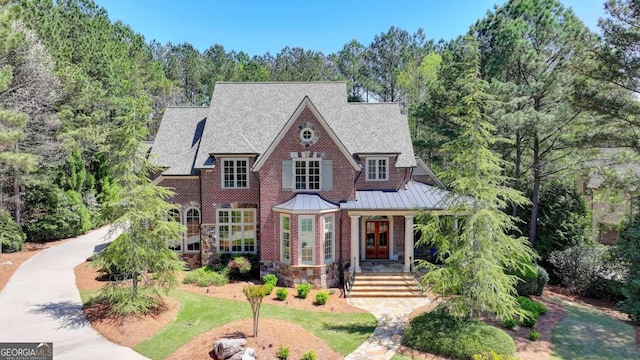 tudor home featuring a porch, metal roof, brick siding, french doors, and a standing seam roof