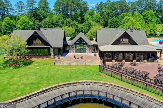 rear view of house with a yard, a patio area, a fenced backyard, and stone siding