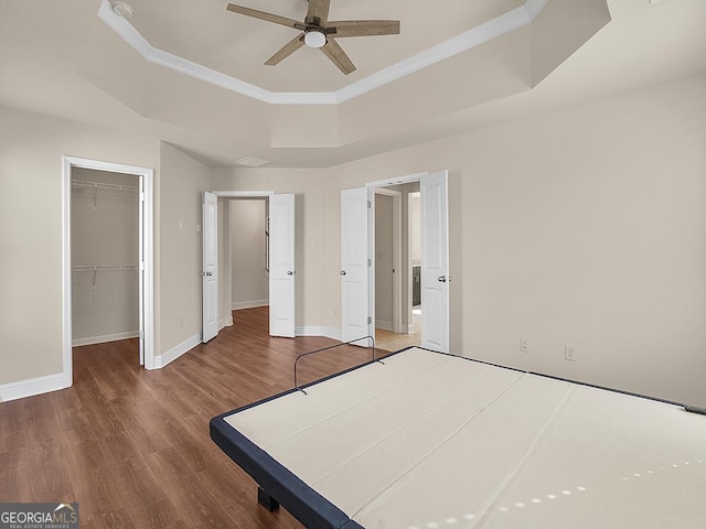 4343 Ainsley Mill Ln, Duluth, GA 30097 - unfurnished bedroom featuring a tray ceiling, baseboards, a walk in closet, and wood finished floors