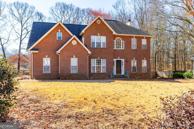 colonial inspired home featuring brick siding, a chimney, and a front lawn