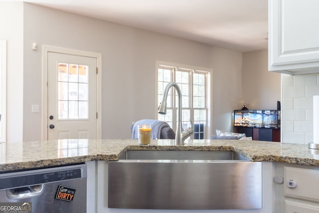 kitchen featuring stainless steel dishwasher, white cabinetry, light stone counters, a sink, and backsplash