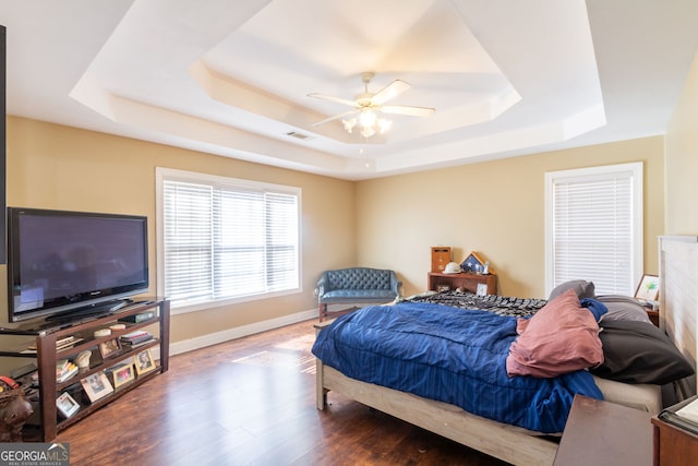 bedroom with a tray ceiling, wood finished floors, baseboards, and visible vents