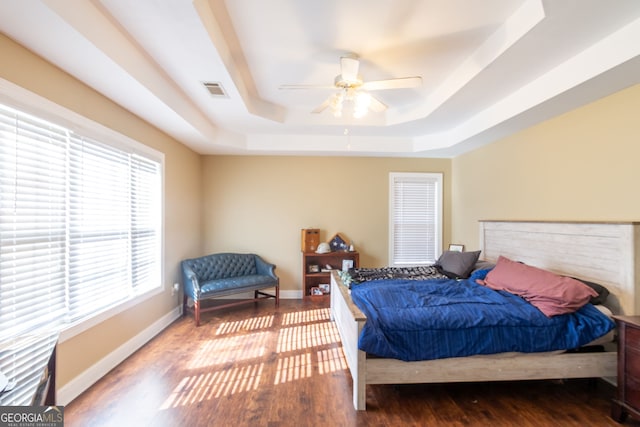 bedroom with visible vents, baseboards, a raised ceiling, ceiling fan, and wood finished floors