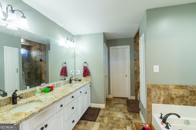 bathroom with a shower stall, stone finish floor, a sink, double vanity, and baseboards