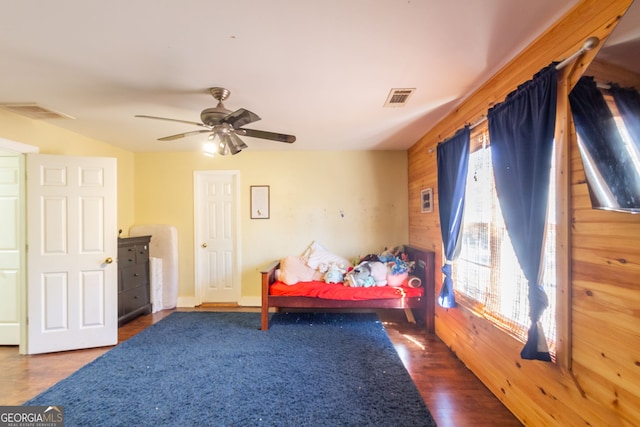 bedroom featuring wooden walls, visible vents, a ceiling fan, and wood finished floors