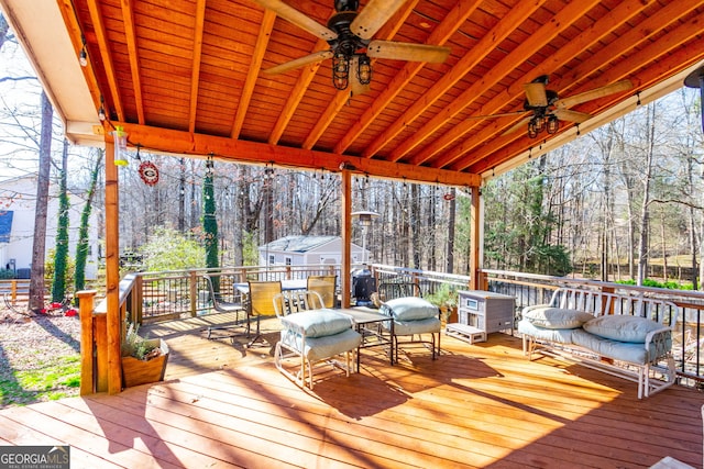 wooden terrace featuring ceiling fan, an outdoor structure, and outdoor dining space