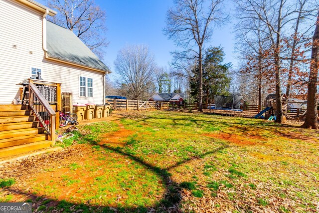 view of yard featuring fence, a trampoline, a wooden deck, and a playground