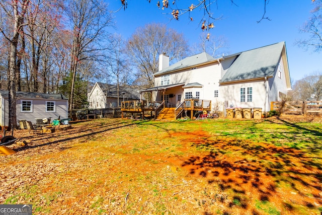 back of property with fence, a deck, a lawn, and a chimney