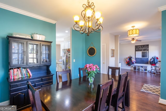 dining area with dark wood-type flooring, ceiling fan with notable chandelier, baseboards, and ornamental molding