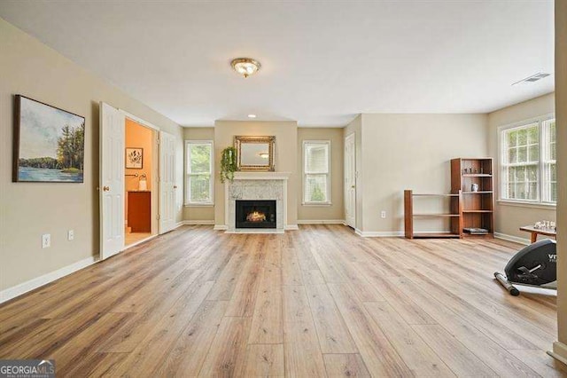 unfurnished living room with light wood-type flooring, plenty of natural light, and baseboards
