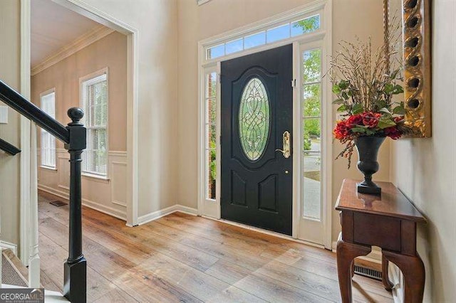 foyer entrance with crown molding, light wood-style flooring, plenty of natural light, and stairway