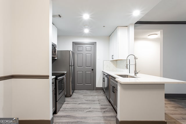 1074 Peachtree Walk NE Unit 115, Atlanta, GA 30309 - kitchen featuring appliances with stainless steel finishes, a peninsula, light wood-type flooring, white cabinets, and decorative backsplash