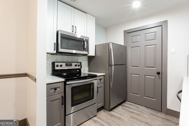 1074 Peachtree Walk NE Unit 115, Atlanta, GA 30309 - kitchen with appliances with stainless steel finishes, light wood-style flooring, decorative backsplash, light countertops, and white cabinetry