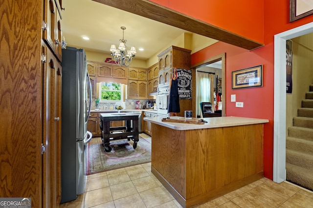 kitchen with freestanding refrigerator, an inviting chandelier, light tile patterned floors, a peninsula, and light countertops