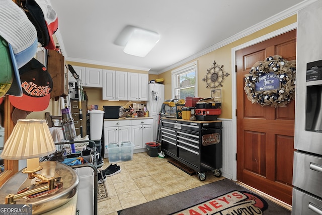 kitchen with white cabinetry, ornamental molding, a wainscoted wall, light countertops, and tile patterned floors