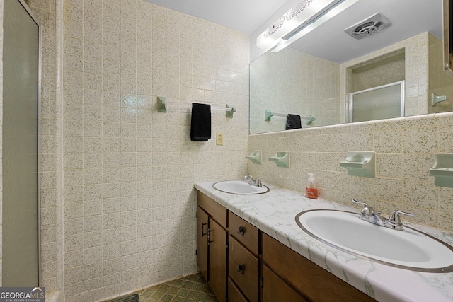 full bath with a shower stall, double vanity, tile walls, and a sink
