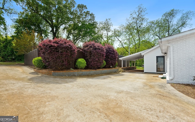 view of yard featuring concrete driveway, an attached carport, and fence