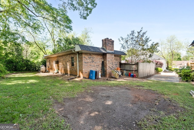 back of house featuring a chimney, brick siding, a yard, fence, and a shingled roof
