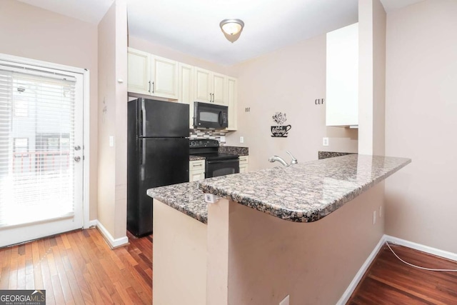 kitchen with light wood-style floors, a peninsula, black appliances, light stone counters, and baseboards