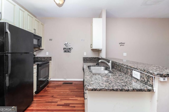 kitchen featuring dark stone countertops, a sink, a peninsula, black appliances, and wood finished floors
