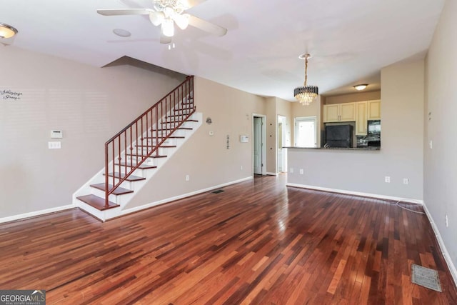unfurnished living room featuring baseboards, stairway, visible vents, dark wood finished floors, and ceiling fan with notable chandelier